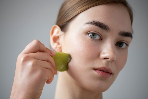 Portrait of beautiful woman with clear skin using guasha to massage her face