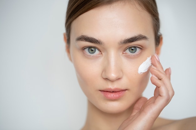 Portrait of beautiful woman with clear skin using moisturizer on her face