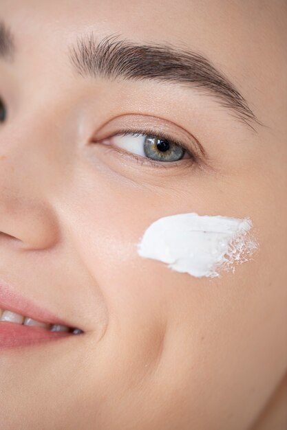 Portrait of beautiful woman with clear skin using moisturizer on her face