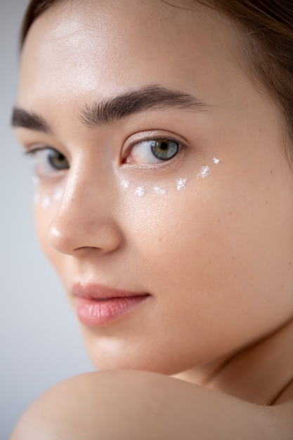 Portrait of beautiful woman with clear skin using moisturizer on her face