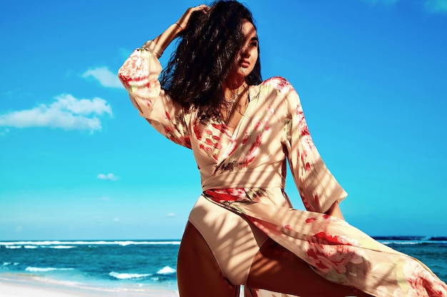 Free photo portrait of beautiful woman with dark long hair in beige dress posing on summer beach