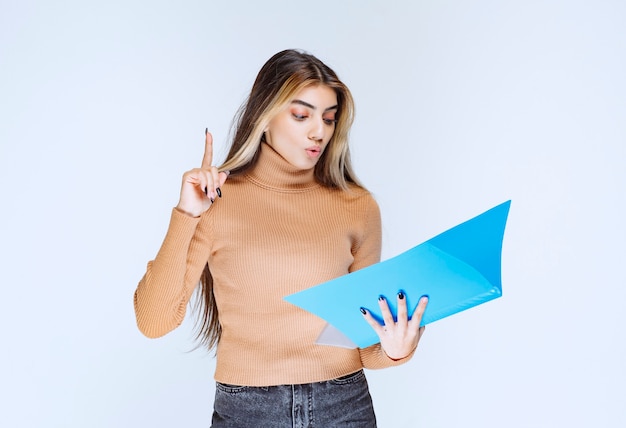 Portrait of a beautiful woman with a folder standing and pointing up .