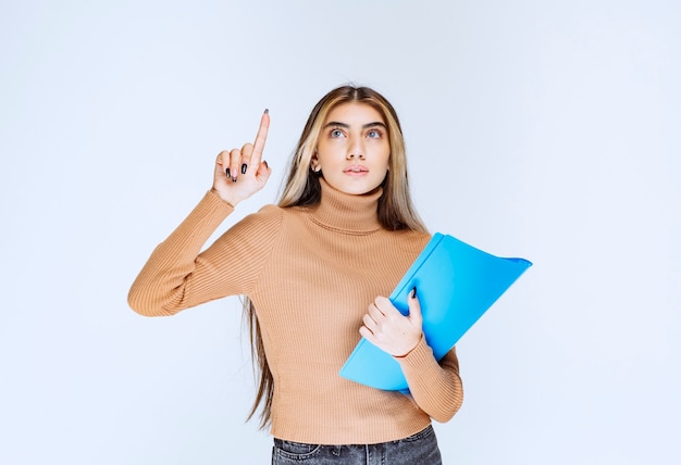 Portrait of a beautiful woman with a folder standing and pointing up .