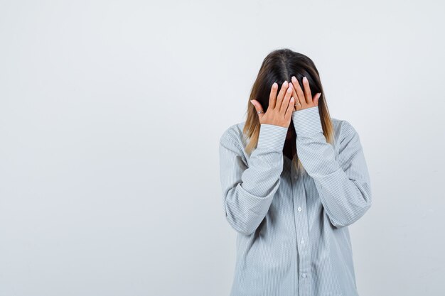 Portrait of beautiful woman with hands on head bent down in shirt and looking depressed front view