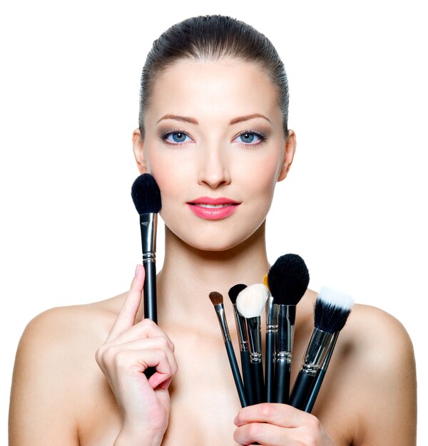 Portrait of the beautiful woman with make-up brushes near attractive face. Adult girll posing over white space