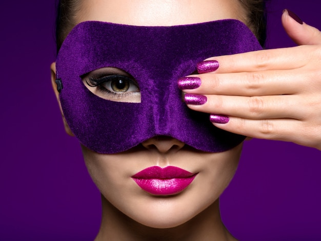 Ritratto di una bella donna con unghie viola e maschera teatrale viola sul viso.