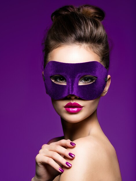 Портрет красивой женщины с фиолетовыми ногтями и театральной маской на лице.