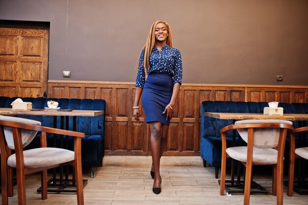 Portrait of beautiful young african business woman with dreadlocks wear on blue blouse and skirt posed in cafe