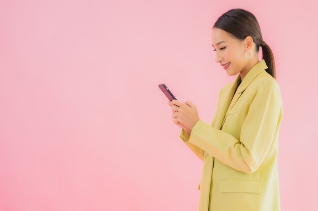 肖像画の美しい若いアジアビジネスの女性は色のコーヒーカップを持つスマートな携帯電話を使用します。