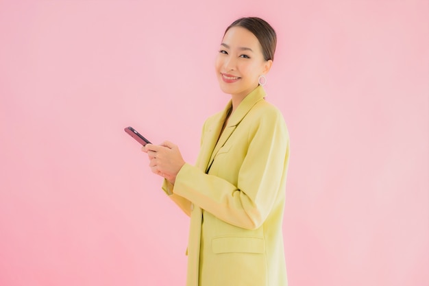 La bella giovane donna asiatica di affari del ritratto usa il telefono cellulare astuto con la tazza di caffè sul colore