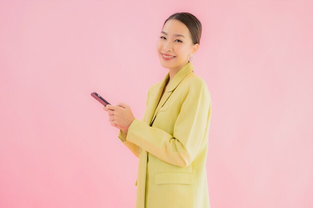 肖像画の美しい若いアジアビジネスの女性は色のコーヒーカップを持つスマートな携帯電話を使用します。