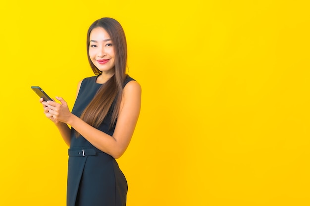 黄色の背景にコーヒーカップとスマート携帯電話と肖像画美しい若いアジアのビジネス女性