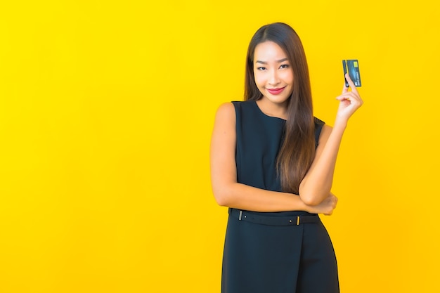黄色の背景にクレジットカードを持つ美しい若いアジアのビジネス女性