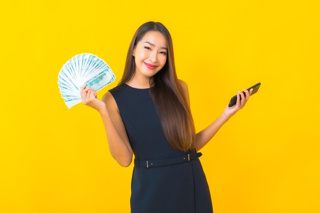 노란색 배경에 현금과 돈을 많이 가진 초상화 아름 다운 젊은 아시아 비즈니스 여자