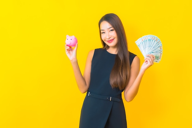黄色の背景にたくさんの現金とお金と肖像画美しい若いアジアのビジネス女性