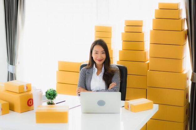 Portrait beautiful young asian business woman work from home with laptop mobile phone with cardboard box ready for shipping