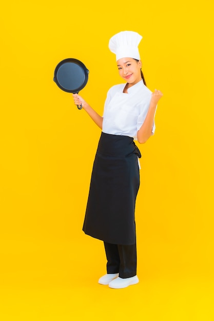 Free photo portrait beautiful young asian chef woman with black pan on yellow isolated background