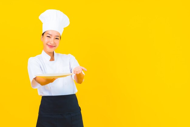 Portrait beautiful young asian chef woman with plate on yellow isolated background