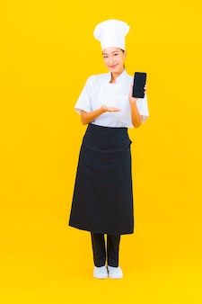 노란색 고립 된 배경에 스마트 휴대 전화와 함께 초상화 아름 다운 젊은 아시아 요리사 여자