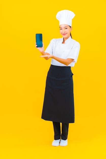 Portrait beautiful young asian chef woman with smart mobile phone on yellow isolated background