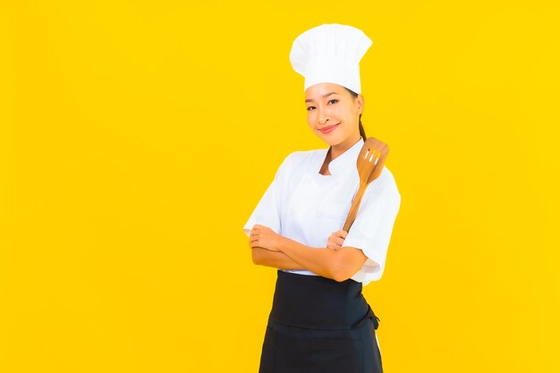 Portrait beautiful young asian chef woman with spatula on yellow isolated background