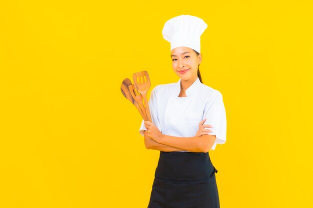 Portrait beautiful young asian chef woman with spatula on yellow isolated background