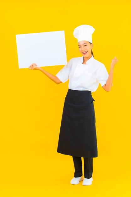 Portrait beautiful young asian chef woman with white empty billboard on yellow isolated background