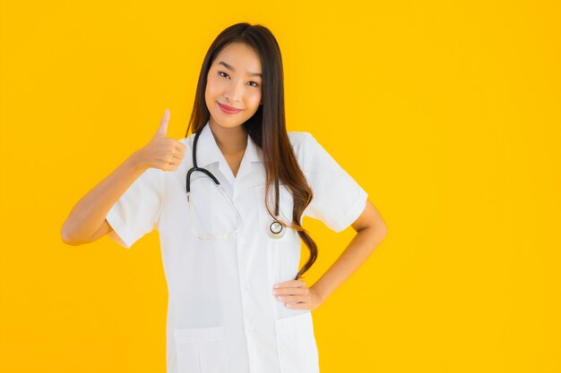 Портрет красивой молодой азиатской женщины доктора усмехается и показывает большой палец руки вверх