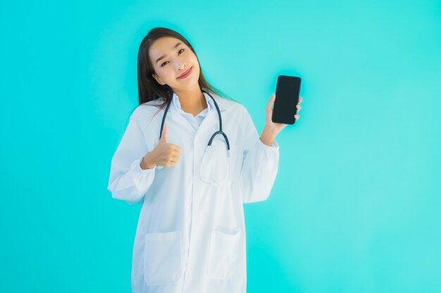 肖像画の美しい若いアジア医師の女性はモバイルスマート携帯電話を使用します。