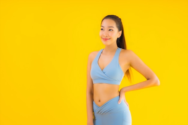 Женщина спорта портрета красивая молодая азиатская готовая для тренировки на желтом цвете