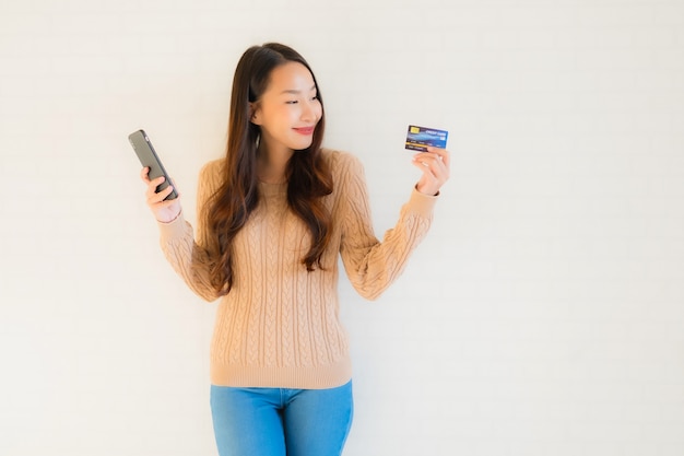 Телефон красивой молодой азиатской пользы передвижной умный с кредитной карточкой
