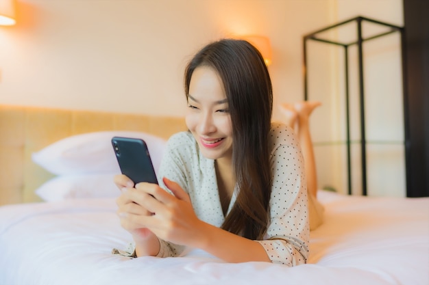 스마트 휴대 전화와 함께 침대에 세로 아름 다운 젊은 아시아 여자