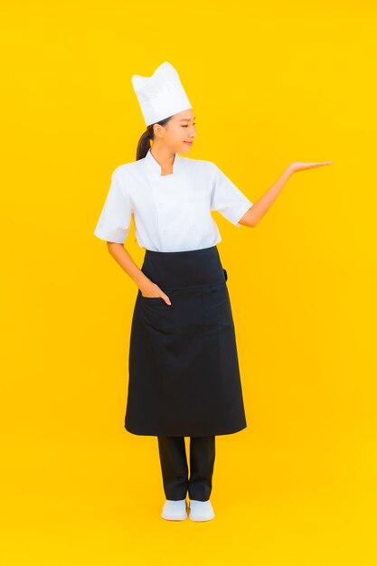 Portrait beautiful young asian woman in chef or cook uniform with hat on yellow isolated background