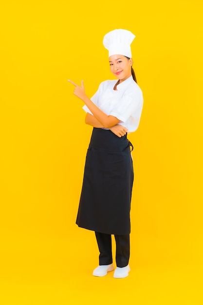 Portrait beautiful young asian woman in chef or cook uniform with hat on yellow isolated background