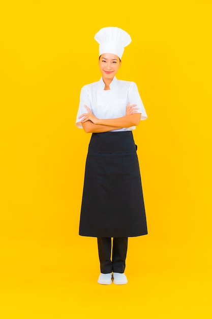 Portrait beautiful young asian woman in chef or cook uniform with hat on yellow isolated background