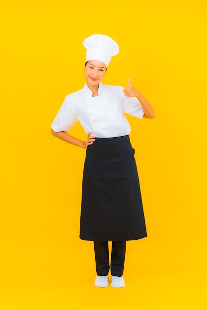 Portrait beautiful young asian woman in chef or cook uniform with hat on yellow isolated background