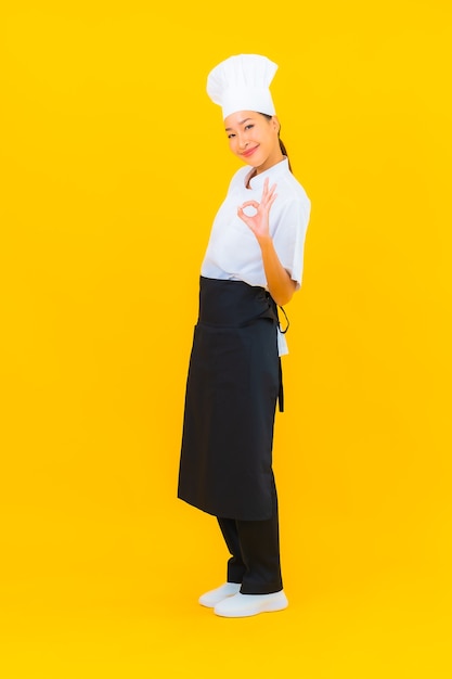 Portrait beautiful young asian woman in chef or cook uniform with hat on yellow isolated background