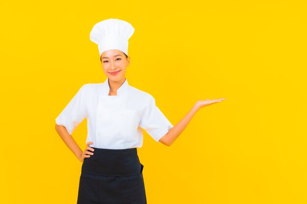 Portrait beautiful young asian woman in chef or cook uniform with hat on yellow isolated background