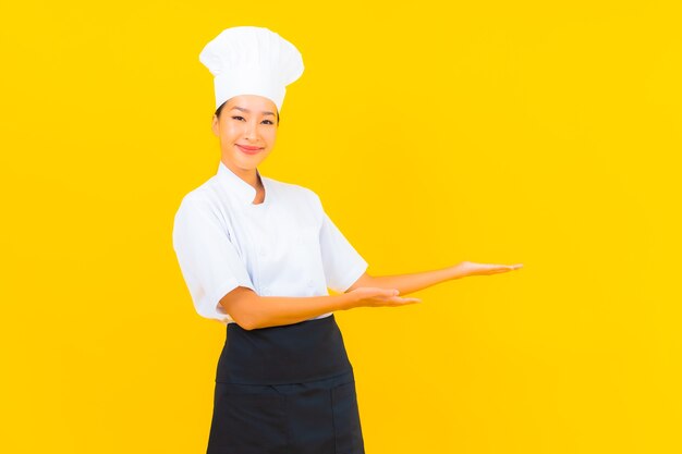 Portrait beautiful young asian woman in chef or cook uniform with hat on yellow isolated background