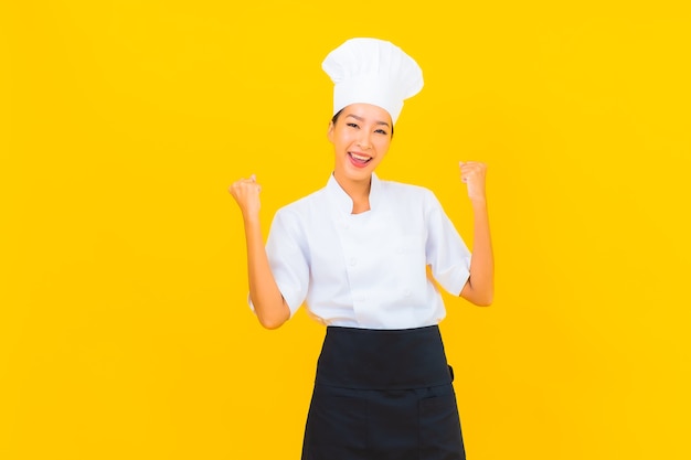 노란색 외진 배경에 모자를 쓴 요리사 또는 요리사 유니폼을 입은 아름다운 젊은 아시아 여성의 초상화