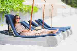 Free photo portrait beautiful young asian woman on the deck chair with umbrella around beach sea ocean