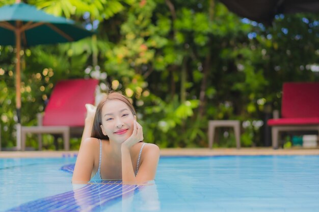 세로 아름 다운 젊은 아시아 여자는 호텔에서 야외 수영장 주변의 미소 레저 휴식을 즐길 수