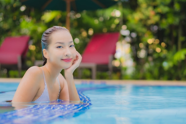 Женщина портрета красивая молодая азиатская наслаждается расслабленным отдыхом улыбки вокруг открытого бассейна в гостинице