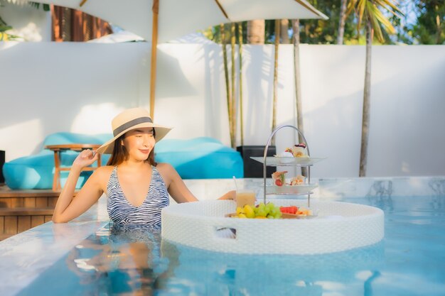 Foto gratuita la bella giovane donna asiatica del ritratto gode di con il tè o la prima colazione di pomeriggio che galleggia sulla piscina