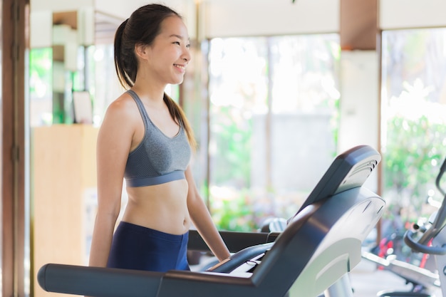 Тренировка женщины портрета красивая молодая азиатская с оборудованием фитнеса в интерьере спортзала