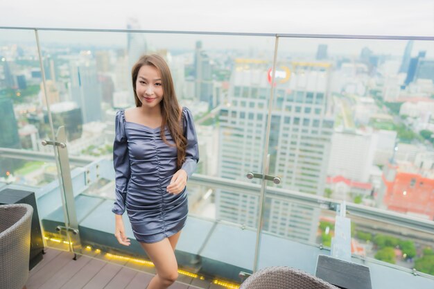 Бесплатное фото Улыбка красивой молодой азиатской женщины портрета счастливая на ресторане на крыше вокруг вида на город