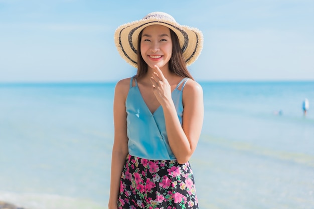 Улыбка красивой молодой азиатской женщины портрета счастливая ослабляет вокруг океана и моря пляжа
