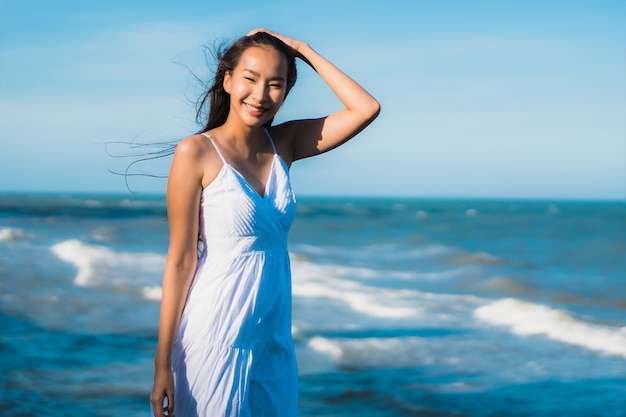Улыбка красивой молодой азиатской женщины портрета счастливая ослабляет около пляжа и моря Neary