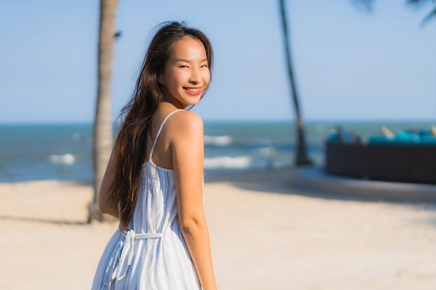 Il sorriso felice della bella giovane donna asiatica del ritratto si rilassa intorno alla spiaggia ed al mare vicini