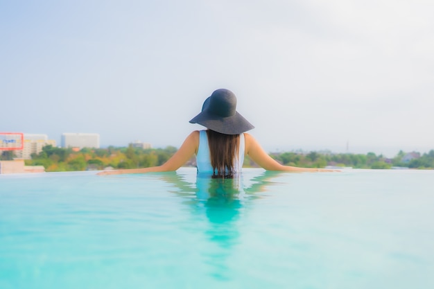 Foto gratuita il sorriso felice della bella giovane donna asiatica del ritratto si rilassa intorno alla piscina all'aperto nella località di soggiorno dell'hotel